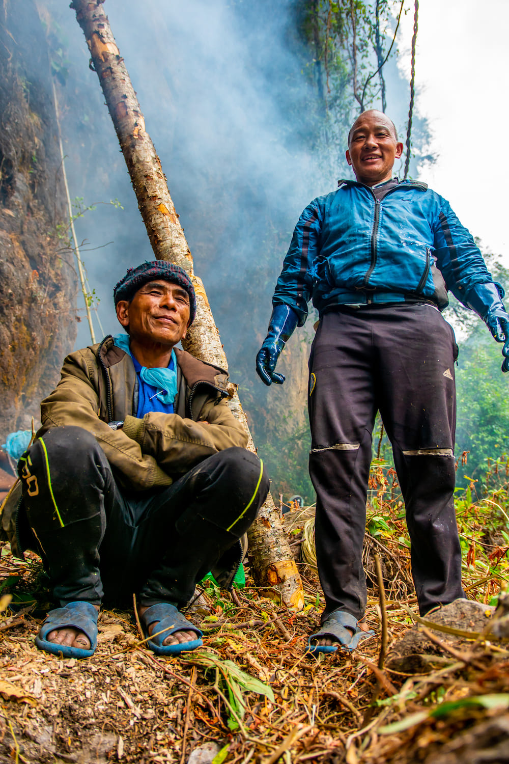 Two honey hunter smiling men standing in forest smoke